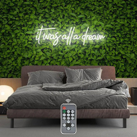 Bedroom with 'It Was All A Dream' neon sign, LED wall decor 27x8.5 inch, remote control, on green leafy background.