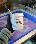 Person holding White Plastisol Screen Printing Ink, Fast Cure At 270F, 32oz Quart, EZ To Use Fabric Paint in front of screen