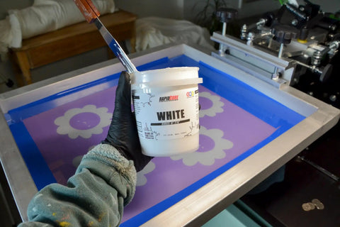Person holding White Plastisol Screen Printing Ink, Fast Cure At 270F, 32oz Quart, EZ To Use Fabric Paint in front of screen
