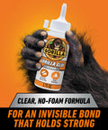 Front view of Gorilla Glue Clear adhesive bottle, 3.75 oz, white cap, orange label, held by gloved hand
