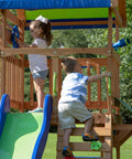 Children playing on Beachfront Cedar Wood Swing Set With Wave Slide Elevated Deck Canopy Monkey Bars Rock Wall Ladder Shaded Picnic Area Snack Bar Window Belt Swings Trapeze Sandbox Playset For Kids