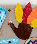 Thanksgiving turkey craft made with colored duct tape and paper feathers on a bulletin board with party invitations.