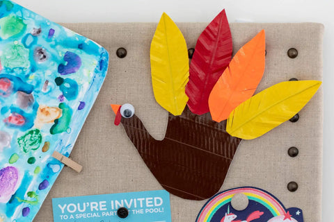 Thanksgiving turkey craft made with colored duct tape and paper feathers on a bulletin board with party invitations.