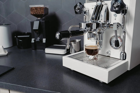 Next Level Home Bar Essentials Italian Handcrafted Espresso Machine With Heat Exchanger And E61 Manual Controls Badass Stainless Steel Chassis Three Liter Tank Fresh White Finish Straight Fire Quality For Every Coffee Geek brewing espresso shot on kitchen countertop.
