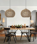 Dining room with two One Light Rattan Woven Pendant Light Fixture With Handwoven Lampshade Handmade Ceiling Chandelier In Farmhouse Style Natural Seagrass Shade For LED Edison CFL Bulbs 13.7 Inch Wide, hanging above a wooden table with black chairs.