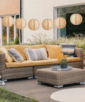 Outdoor patio with 12 Pack 8 Inch Burlap Paper Lanterns Round Chinese Lanterns for Farmhouse Boho Home Decor hanging above wicker sofa.