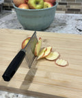 Side view of stainless steel crinkle-cut blade slicer with black handle slicing an apple on a wooden cutting board.