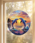 Circular sun catcher with two dolphins at sunset, hanging in a window. Acrylic design with rainbow light effect, 7.4 inch size.
