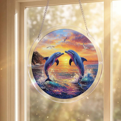 Circular sun catcher with two dolphins at sunset, hanging in a window. Acrylic design with rainbow light effect, 7.4 inch size.
