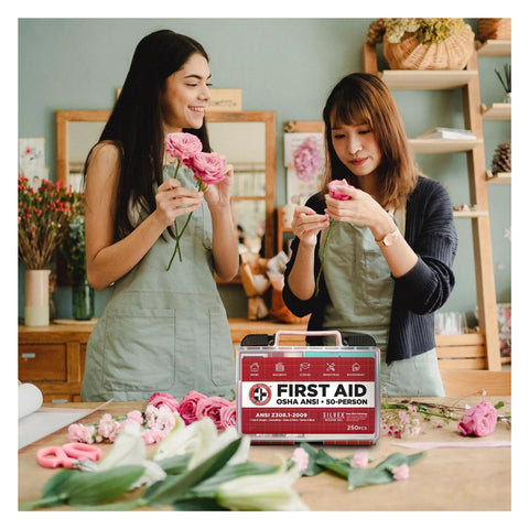 Be Smart Get Prepared OSHA/ANSI First Aid Kit, 50-person, 250-piece case on table; two women with pink flowers.