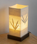 Japanese Lantern Bamboo Table Lamp With Cherry Blossom Accent on wooden surface, warm light glowing through paper shade.