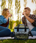 Couple enjoying picnic with Heavy Duty Insulated Cooler Bag With Leakproof Design Soft Portable Lunch Tote, Oxford cloth exterior.