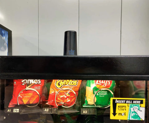 Straight Plug N Go 4G And 5G MIMO Wireless Antenna With Low Profile Panel Mount Setup above snack bags in a vending machine.