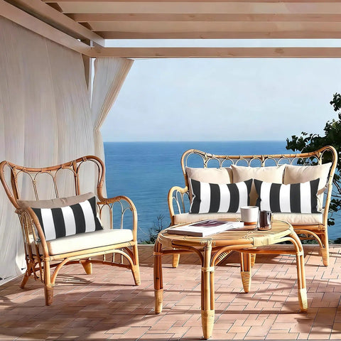 Outdoor Indoor Lumbar Pillows Pack Of 2 Cushions For Patio And Home Sofa Use Water Repellent Fluffy All Weather Cushions 12x20 Inch Cabana Black showcased on wicker patio furniture with ocean view.