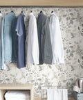 Breezy Peel And Stick Botanical Wallpaper In Gray behind hanging clothes, showcasing modern silhouette design in a closet setting.