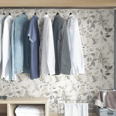 Breezy Peel And Stick Botanical Wallpaper In Gray behind hanging clothes, showcasing modern silhouette design in a closet setting.
