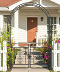 Garden Arbor With Gate Metal Arch Trellis for Climbing Plants and Vines in front of a house with flowers