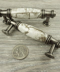 Decorative cabinet pulls with marble design and silver finish next to a quarter for size perspective