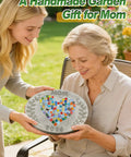 Person holding a handmade gift garden stepping stone with heart mosaic design and the word 'Mom' visible, outdoors.