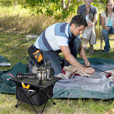 Ultralight Foldable Camping Side Table With Aluminum Build next to a person setting up a tent outdoors.