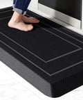 Ridiculously Thick Anti Fatigue Kitchen Mat For Standing Desks And Workstations Waterproof High Density Foam Non Slip Ergonomic Comfort Mat Black 20 By 39 Inches, shown in front of a sink with feet.