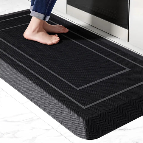 Ridiculously Thick Anti Fatigue Kitchen Mat For Standing Desks And Workstations Waterproof High Density Foam Non Slip Ergonomic Comfort Mat Black 20 By 39 Inches, shown in front of a sink with feet.
