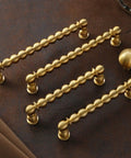 Bead Cabinet Pulls in Brushed Brass With Ball Knobs, Dope Look Gold Kitchen Hardware, Vintage Modern Drawer Handles displayed on leather