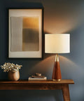 Mid Century Modern Table Lamp With Pecan Wood Base And Gold Metal Accents, White Drum Shade, 26 Inch Tall, in bedroom setting
