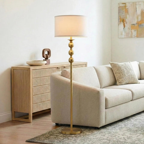 Riley 60 Inch Floor Lamp With Drum Shade In Gold Brass Finish For Living Room Or Bedroom Modern Standing Lamp With Boho Chic Mid Century Vibe And Elegant Corner Light For Office next to a beige sofa.
