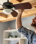 Man adjusting the ceiling fan, showcasing the style of Twenty Piece Heavy Duty Ceiling Fan Blade Screws Quarter Twenty Thread By Three Eighth Inch Long Carbon Steel Pan Head Bolts Copper Finish Locks Right In Zero Wobble Residential Gear.