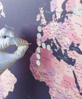 Hand placing Badass 100 Piece Heavy Duty Flat Head Thumb Tack on a colorful world map for display purposes.
