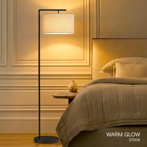 Modern LED Floor Lamp With Tan Fabric Shade Tall Corner Pole Standing Light For Living Rooms And Offices Ideal Bedroom Reading Light Black Finish next to bed with warm glow.