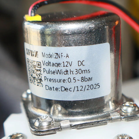 Close-up of model ZNF-A 12V DC solenoid valve with label showing voltage, pulse width, and pressure for smart toilet bidet installation.