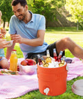 Portable Sports Drink Dispenser With Heavy Insulation Keeps Backyard Faves Stay Frosty All Weekend And Sip Smooth At Tailgates While Hanging Out In Vibrant Orange with drinks in ice during a picnic.