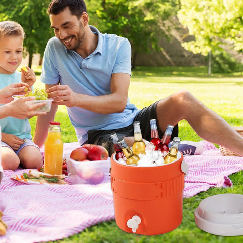 Portable Sports Drink Dispenser With Heavy Insulation Keeps Backyard Faves Stay Frosty All Weekend And Sip Smooth At Tailgates While Hanging Out In Vibrant Orange with drinks in ice during a picnic.