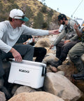 Latitude Marine Ultra White 25 Quart Cooler With Cool Riser Technology ThermoCool Foam Insulation on rocks near fishing group