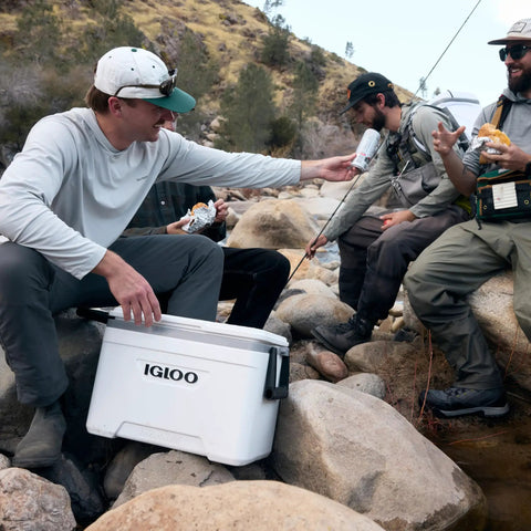 Latitude Marine Ultra White 25 Quart Cooler With Cool Riser Technology ThermoCool Foam Insulation on rocks near fishing group