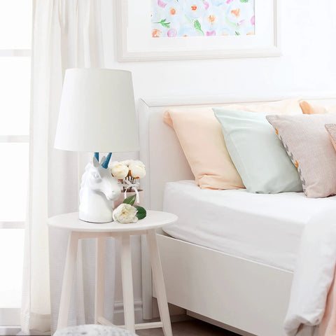 Totally Sparkly Pink Unicorn Table Lamp With Glitter Resin Base And White Tapered Shade on nightstand beside bed.