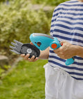 Person holding a cordless hedge trimmer and grass shears, battery powered handheld electric garden tool with ergonomic design.