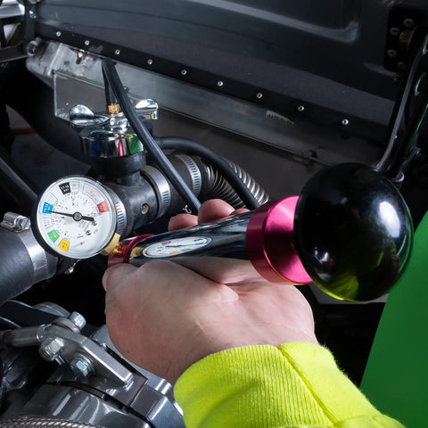 Person using Cooling System Pressure Test Pump Kit For Cars And Trucks, showing gauge and hose connection in engine bay.