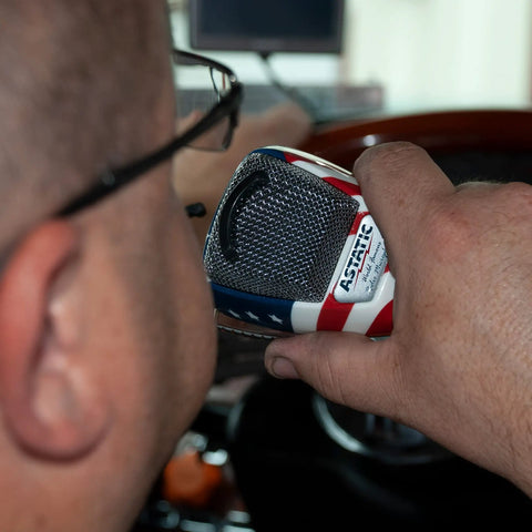 Person using Stars N Stripes Noise Canceling 4 Pin CB Microphone with rugged chrome grille in a vehicle setting.