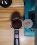 53.5mm Espresso Puck Screen Reusable 1.7mm Thick 100 Micron Stainless Steel Filter Mesh Plate on wooden counter next to portafilter