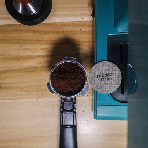 53.5mm Espresso Puck Screen Reusable 1.7mm Thick 100 Micron Stainless Steel Filter Mesh Plate on wooden counter next to portafilter