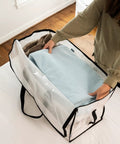Person placing a blue blanket into an Oversized Moving Bags With Backpack Straps Heavy Duty Storage For Moving Dorms And Home Use Ultra