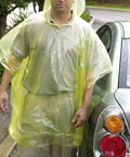 Man wearing yellow rain poncho next to car reflecting light rain