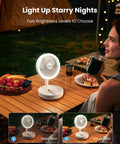 Foldable Desk Fan With LED Night Light 6.8 Inch Wireless Portable Fan at night on a table, person holding a drink outdoors.