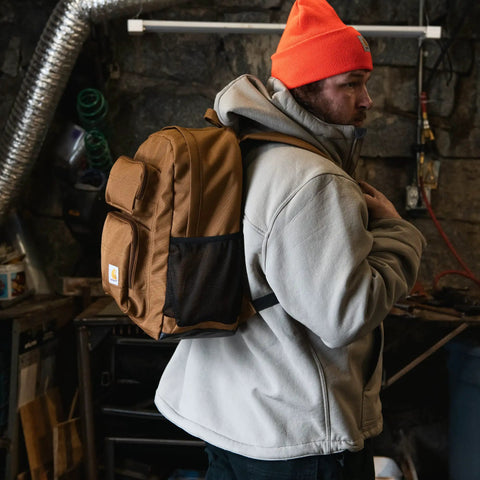 Man wearing 27L Single Compartment Laptop Backpack With Durable Duravax Base Rain Defender Water Repellent 1200 Denier Polyester Built For The Daily Grind On The Go For Work School Or Travel Laptop Sleeve Included, in a workshop setting.