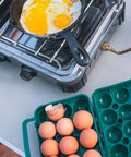Tough 12-Egg Plastic Carrier With Locking Lid and eggs beside a pan on a camping stove