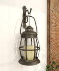Rustic Metal Wall Sconce Lantern With Suspended Pillar Design Brown Glass Finish For Farmhouse Boho Eclectic Interiors Vibe 7 Inch By 10 Inch By 19 Inch Wall Mount Light, showing candle holder against wall.