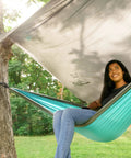 Woman relaxing in a hammock under a Waterproof Hammock Rain Fly Tarp With Stakes And Carry Bag For Backpacking Ultralight Camping Shelter